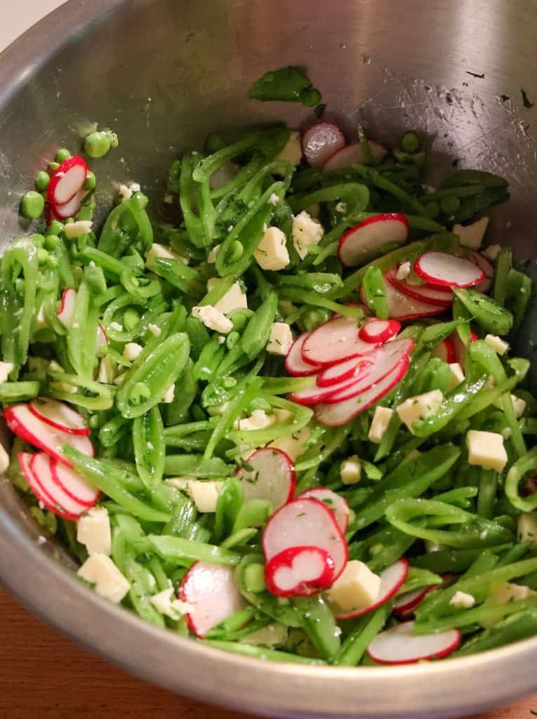 metal bowl filled with sliced snap peas, radishes, feta