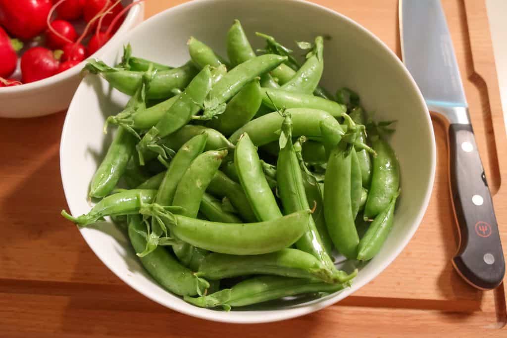 a white bowl on a wooden cutting board filled with snap peas