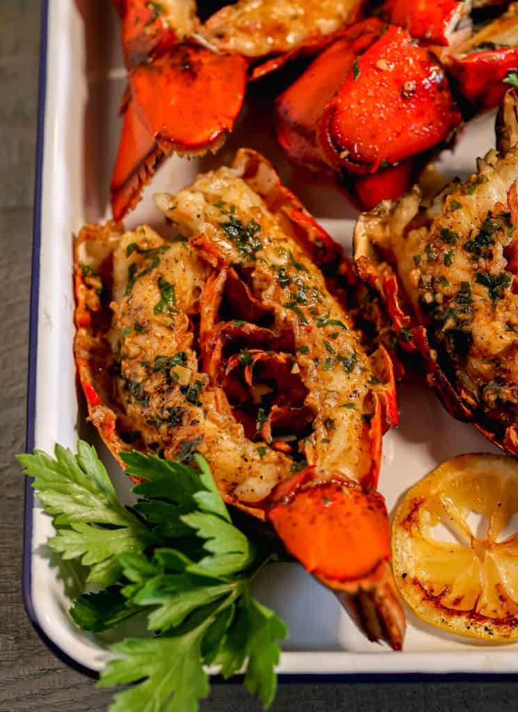 close up of grilled split open lobster tail covered in garlic herb butter