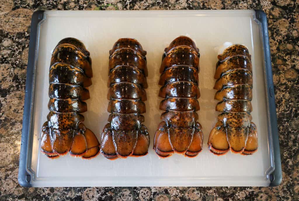 Four lobster tails on a white cutting board, uncooked