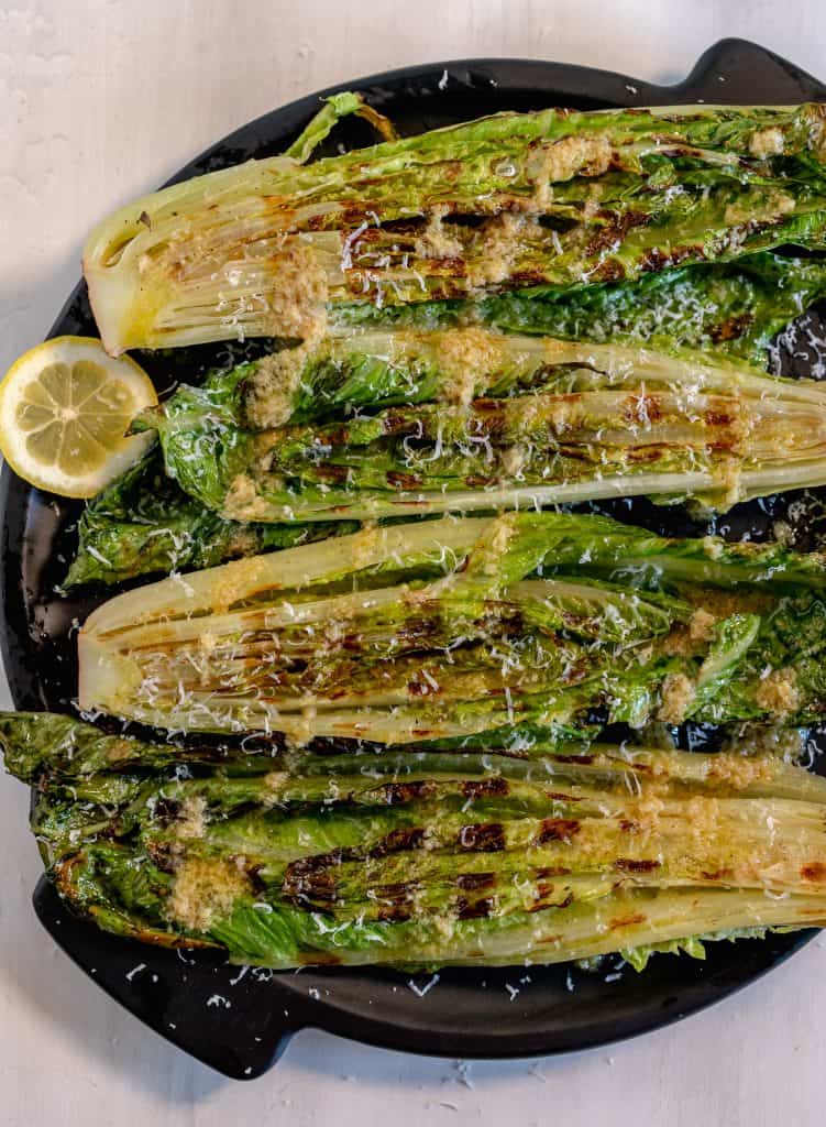Grilled heads of romaine on a black circle plate with sliced lemons surrounding plate