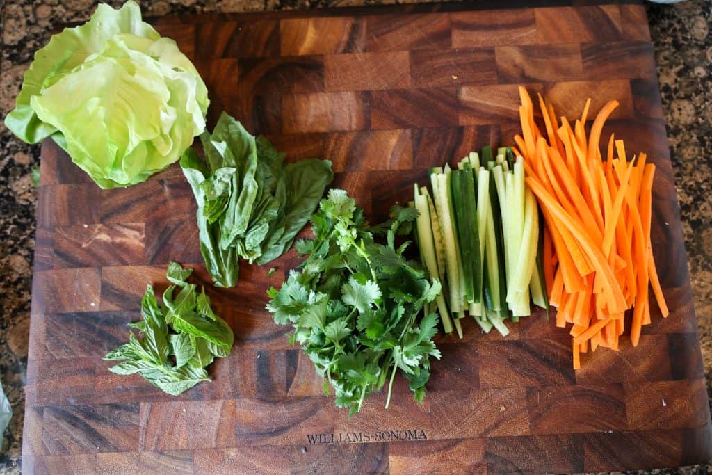 chopped carrots, cucumbers, herbs and lettuce on a wooden cutting board
