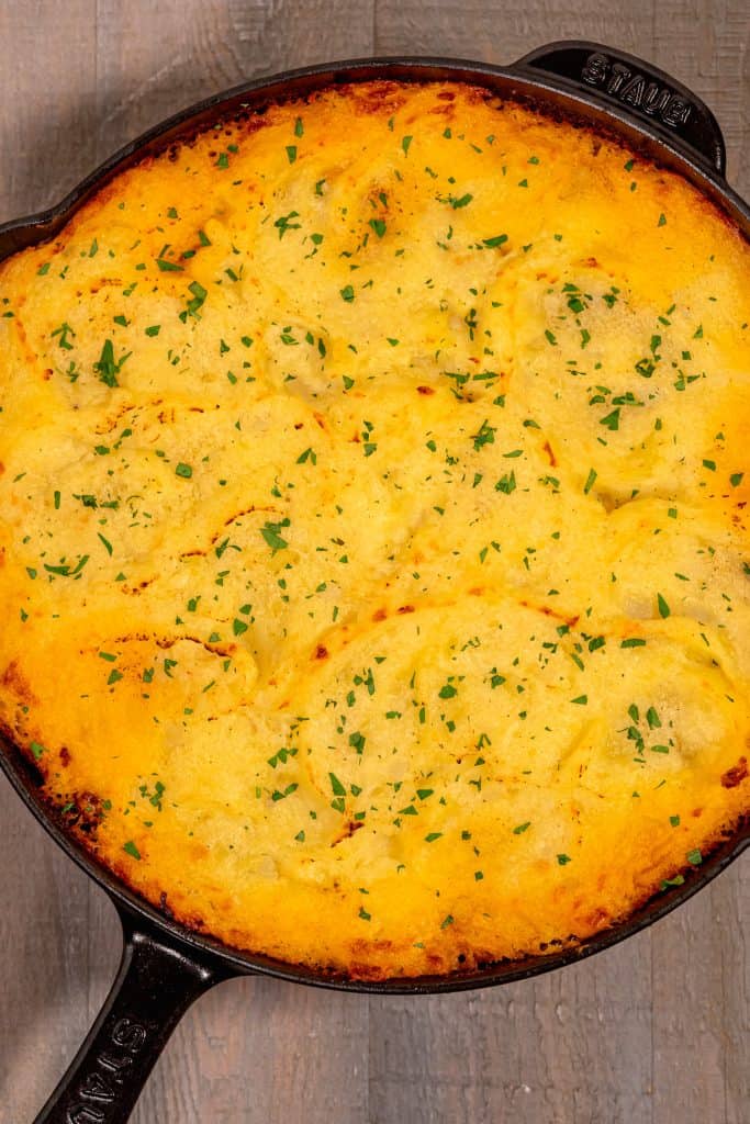 overhead photo of the top of a shepherds pie in a cast iron with golden brown mashed potato as the top layer.
