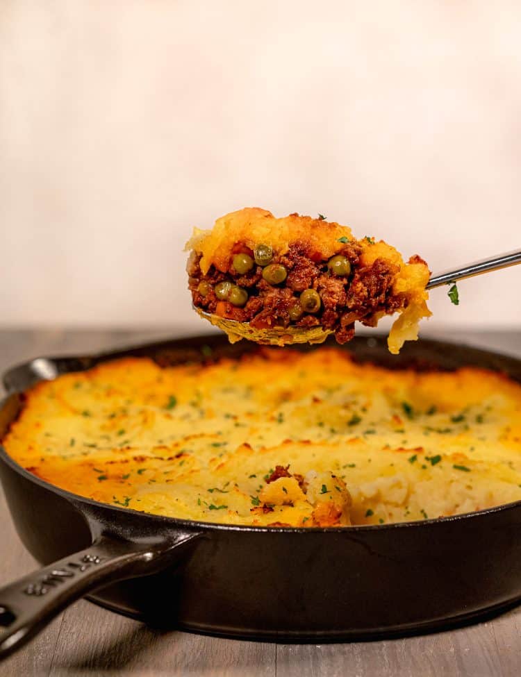 Cast iron skillet with shepherds pie inside and a spoon full being lifted out of the pan