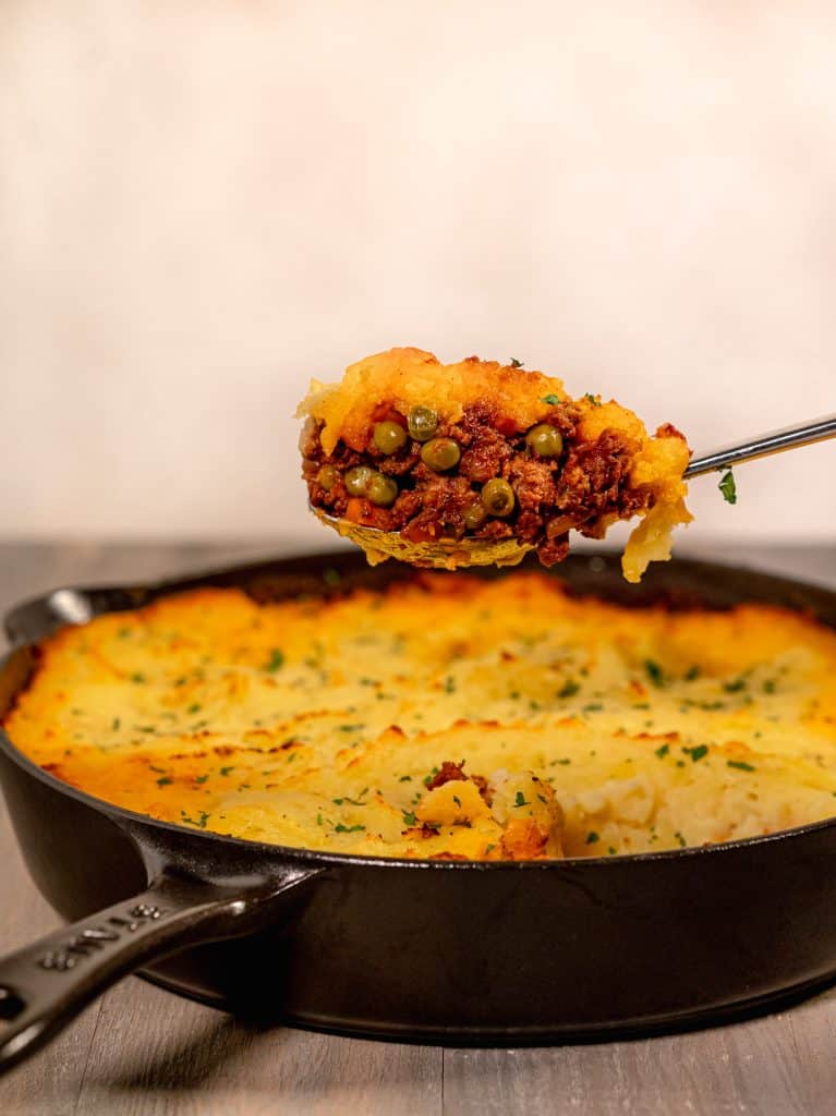 Cast iron skillet with shepherds pie inside and a spoon full being lifted out of the pan 