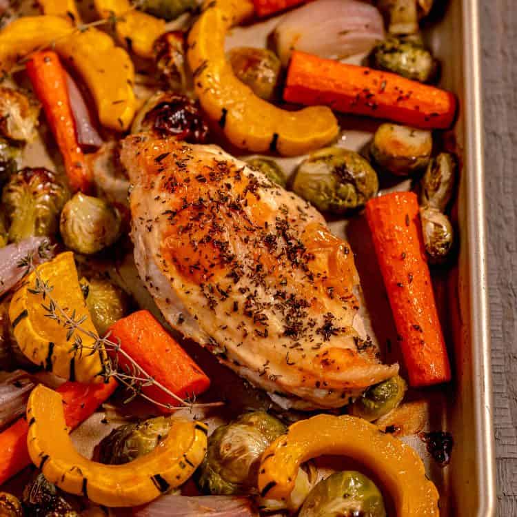 Gold sheet pan filled with a chicken breast, delicata squash slices, carrots, and brussels sprouts