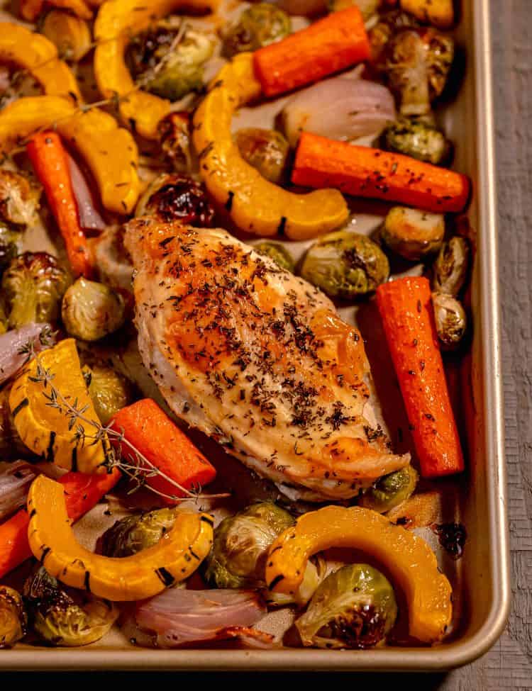 Gold sheet pan filled with a chicken breast, delicata squash slices, carrots, and brussels sprouts