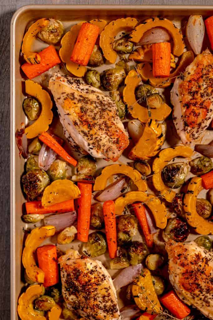 Gold sheet pan filled with a chicken breast, delicata squash slices, carrots, and brussels sprouts