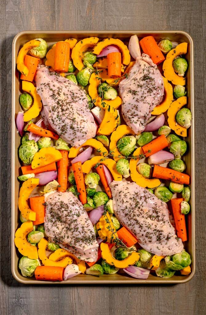 sheet pan of chicken surrounded by brussels sprouts, carrots, squash, and shallots