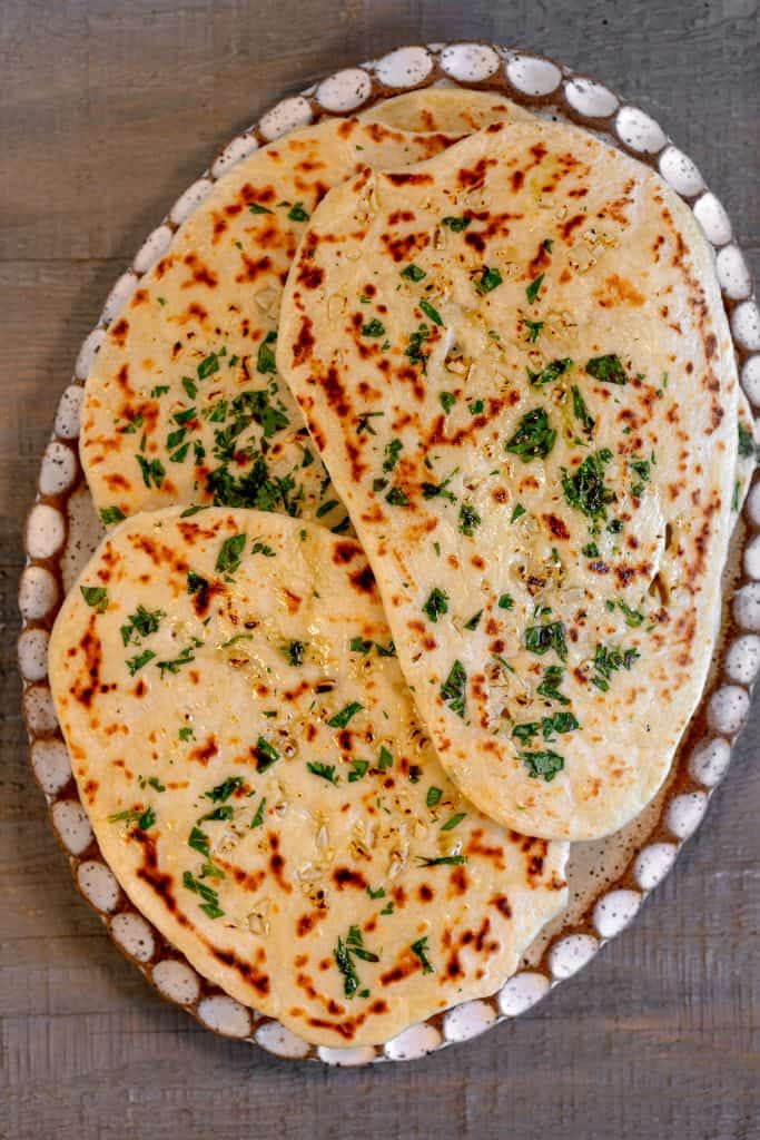 an oval plate on a grey wooden background with garlic naan piled on top of the plate