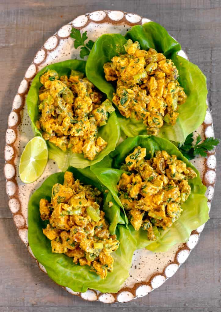 curry chicken salad on lettuce cups on a white oval plate on a wooden background