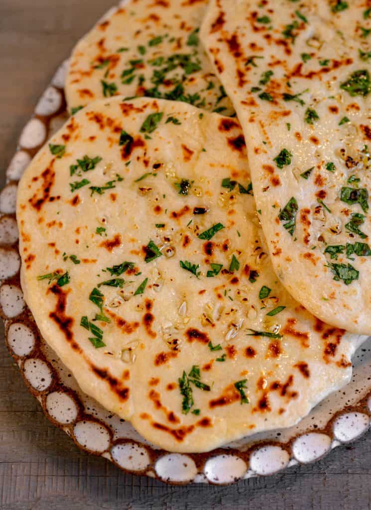 an oval plate on a grey wooden background with garlic naan piled on top of the plate