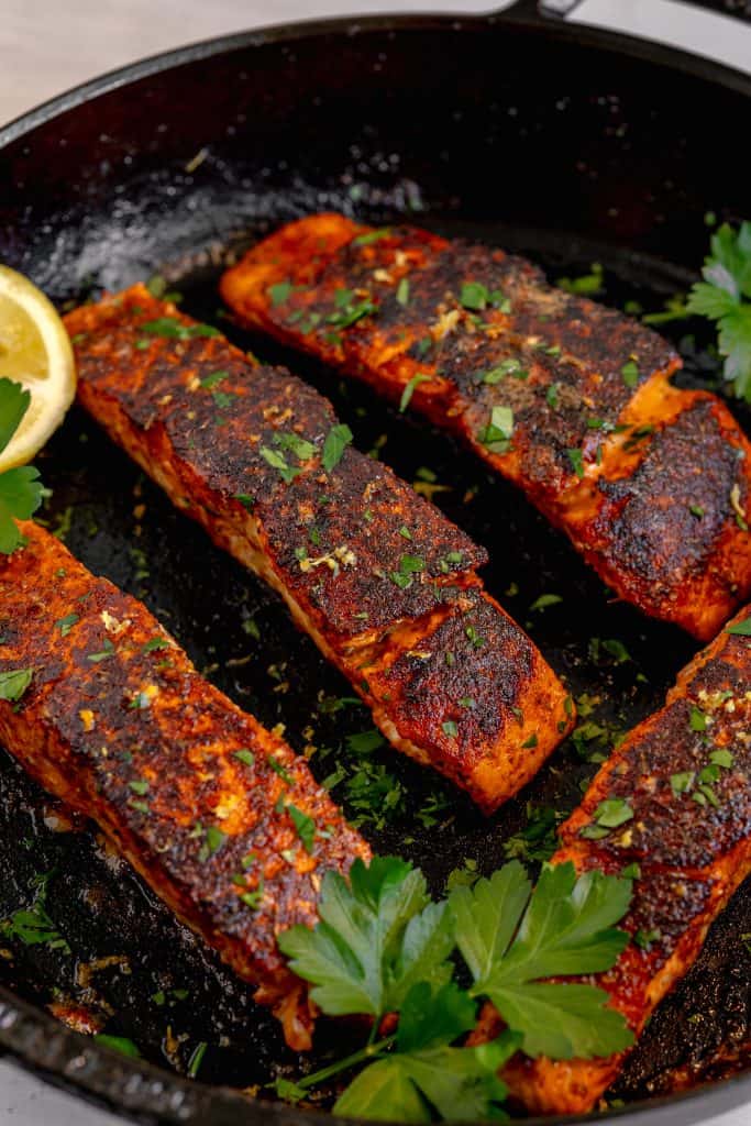 zoomed in on a blackened salmon filet in a cast iron skillet topped with parsley