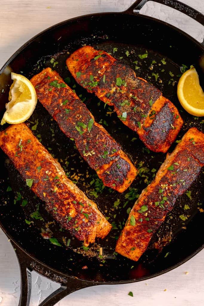 4 salmon filets in a cast iron skillet with two lemon wedges