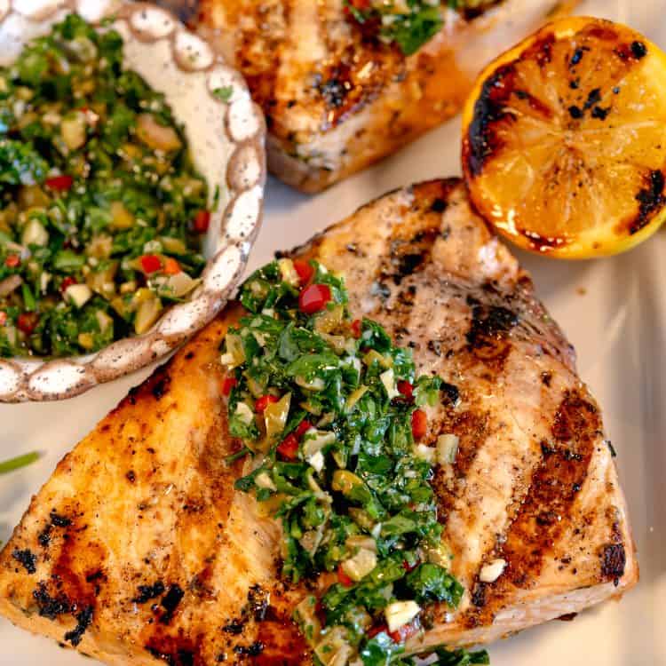 close up of a grilled swordfish steak on a white sheet pan with a charred lemon to the side