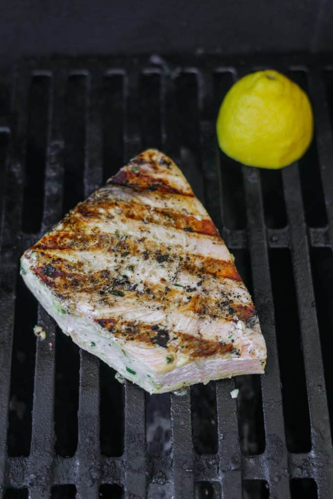 grilling a swordfish steak on a grill with half a lemon in the background