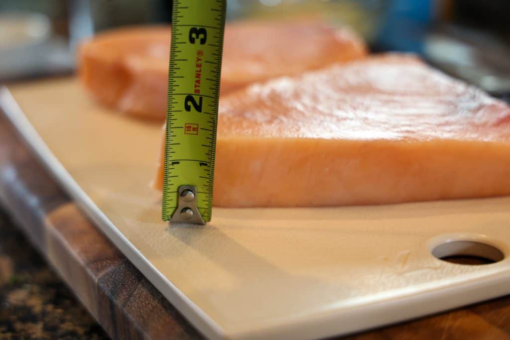 measuring swordfish thickness with a tape measure next to cutting board