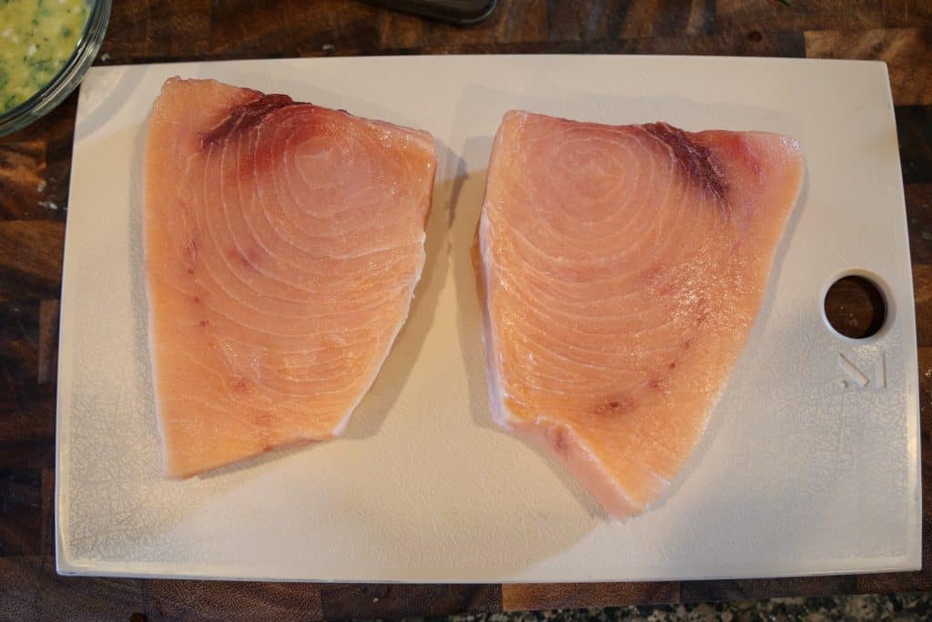 two raw swordfish steaks on a blue cutting board