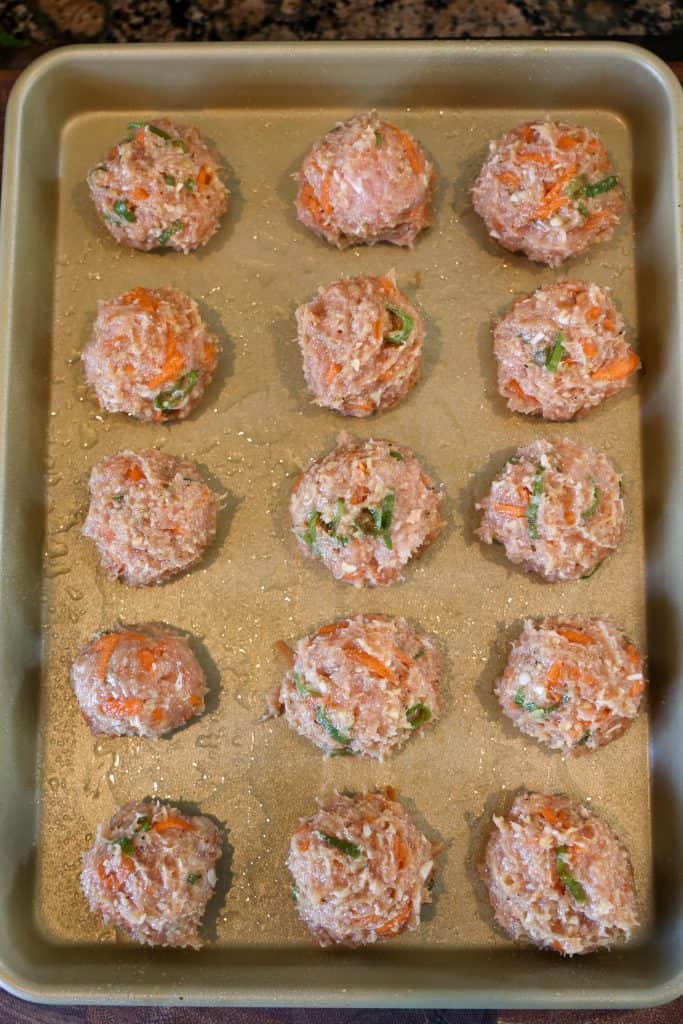 chicken meatballs uncooked on a gold baking sheet