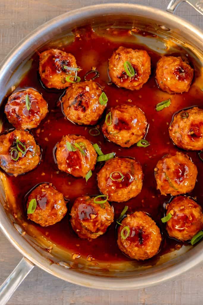 a stainless steal pan filled with chicken meatballs glazed in teriyaki sauce and topped with chopped scallions on a grey background