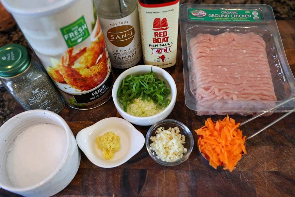 ground chicken, shredded carrots, fish sauce in a bottle, soy sauce in a bottle, panko breadcrumbs on a wooden cutting board