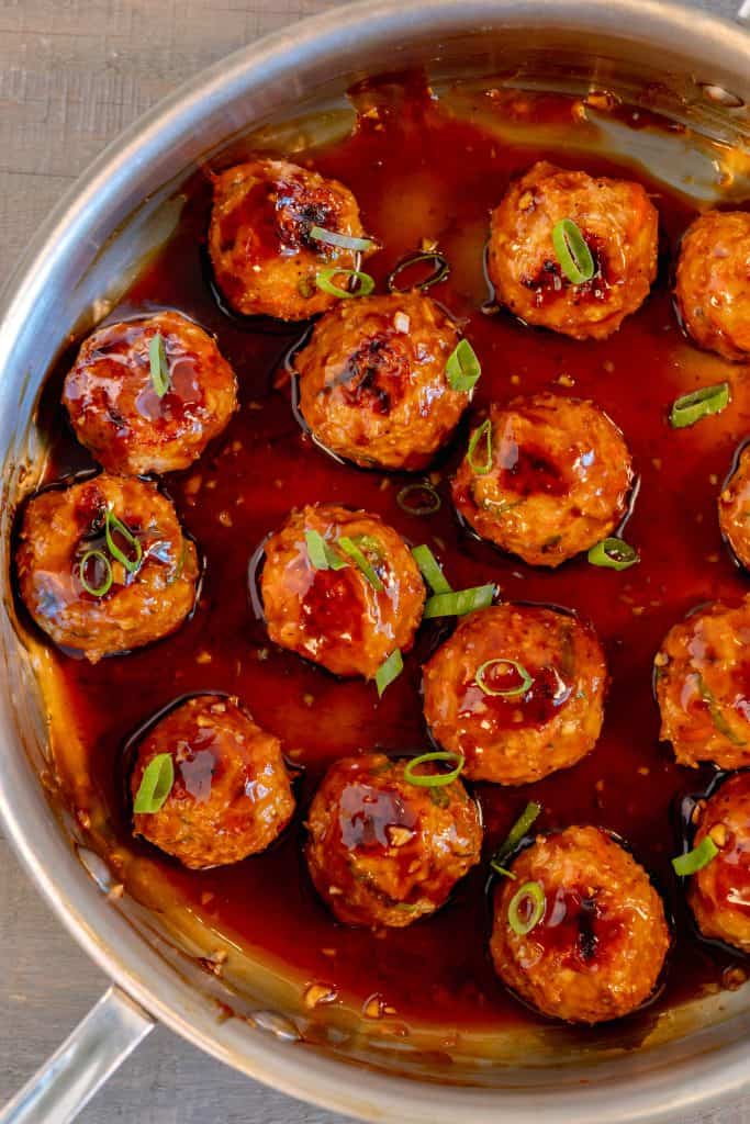 a stainless steal pan filled with chicken meatballs glazed in teriyaki sauce and topped with chopped scallions on a grey background