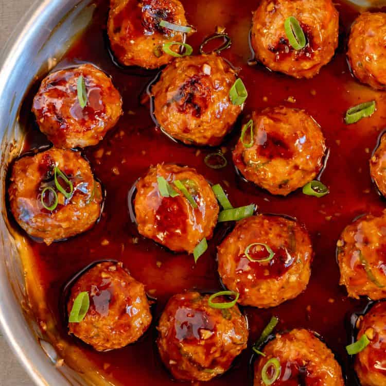 a stainless steal pan filled with chicken meatballs glazed in teriyaki sauce and topped with chopped scallions on a grey background