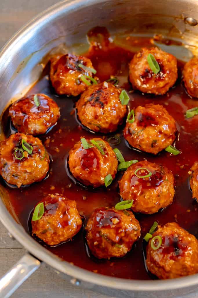 a stainless steal pan filled with chicken meatballs glazed in teriyaki sauce and topped with chopped scallions on a grey background