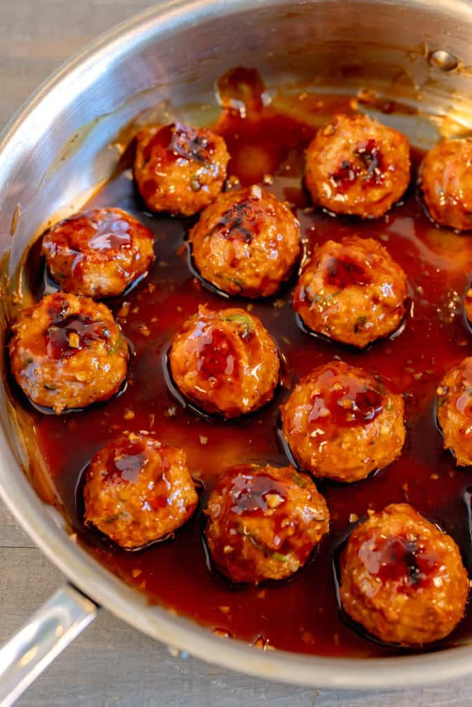 chicken meatballs in a stainless skillet glazed with teriyaki sauce on a grey background