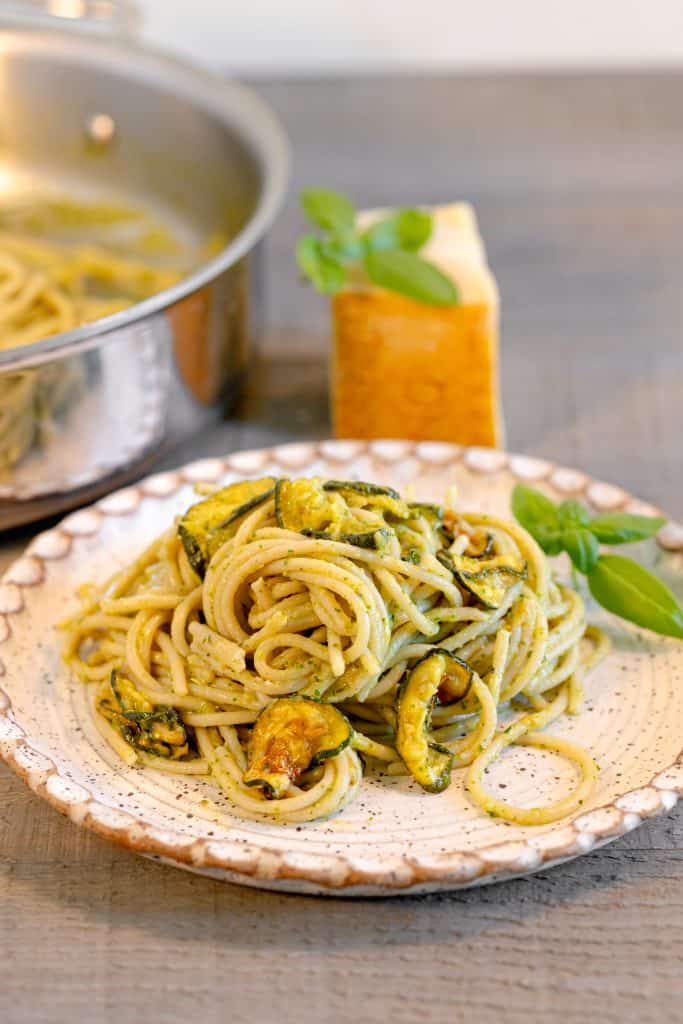 a plate of creamy zucchini pasta with a block of parmesan in the background