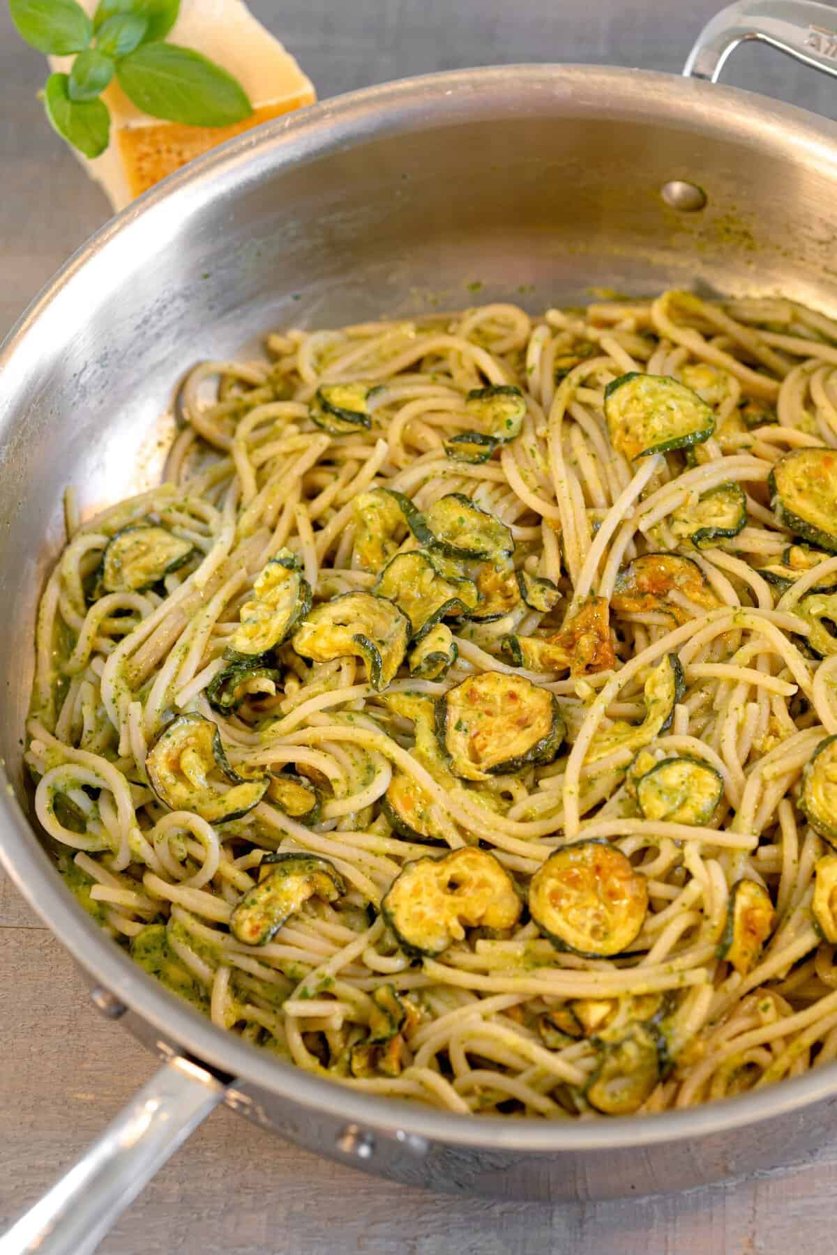 a skillet with creamy zucchini pasta inside of the skillet with a block of parmesan on the background