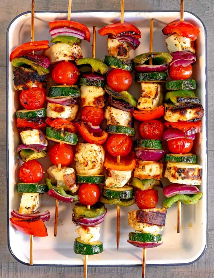 skewers of vegetables and halloumi cheese on a white sheet pan on a grey wooden background