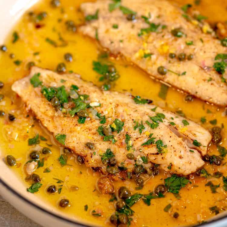 two snapper fish filets in a white skillet covered in a buttery caper sauce