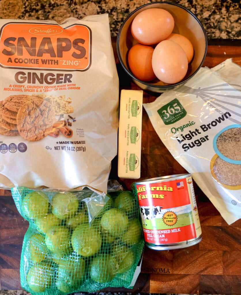bag of gingersnap cookies, bag of key limes, can of condensed milk, bowl of eggs, stick of butter, on a wooden cutting board