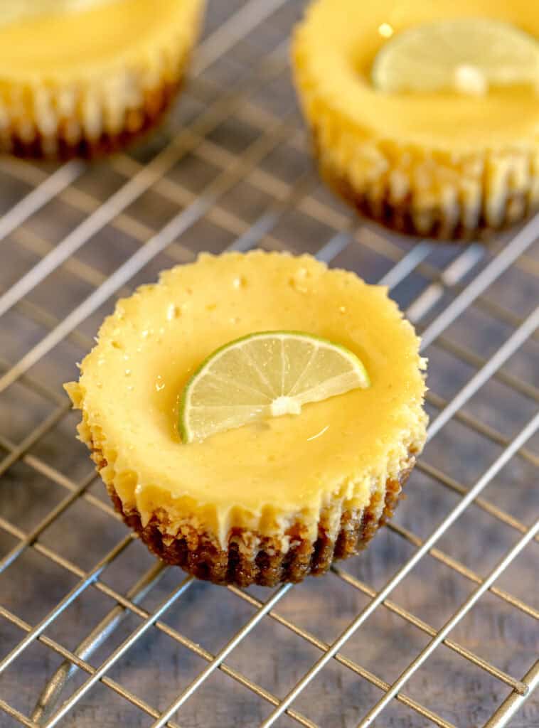 close up of a miniature key lime pie topped with a slice of key lime on a gold cooling rack and grey wooden surface