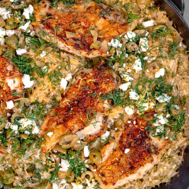 cast iron skillet on a gray wooden background, filled with rice topped with chicken breast, feta cheese, and fresh dill
