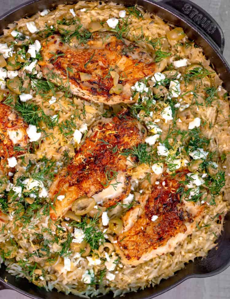 cast iron skillet on a gray wooden background, filled with rice topped with chicken breast, feta cheese, and fresh dill