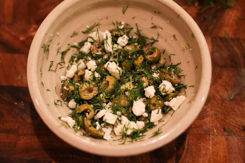 bowl of feta, chopped green olives, and dill on a wooden cutting board